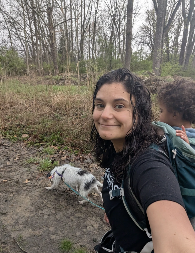 Picture of mom with baby on her back walking a dog.